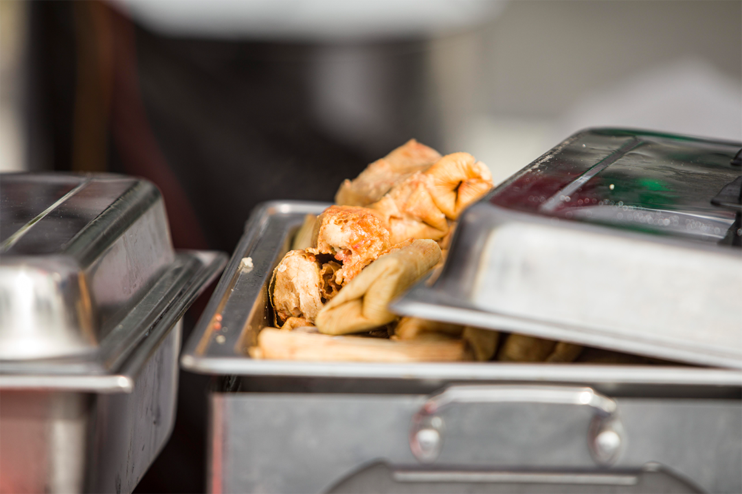 Photo of steaming tamales partially exposed in a silver tray with the lid part of the way off